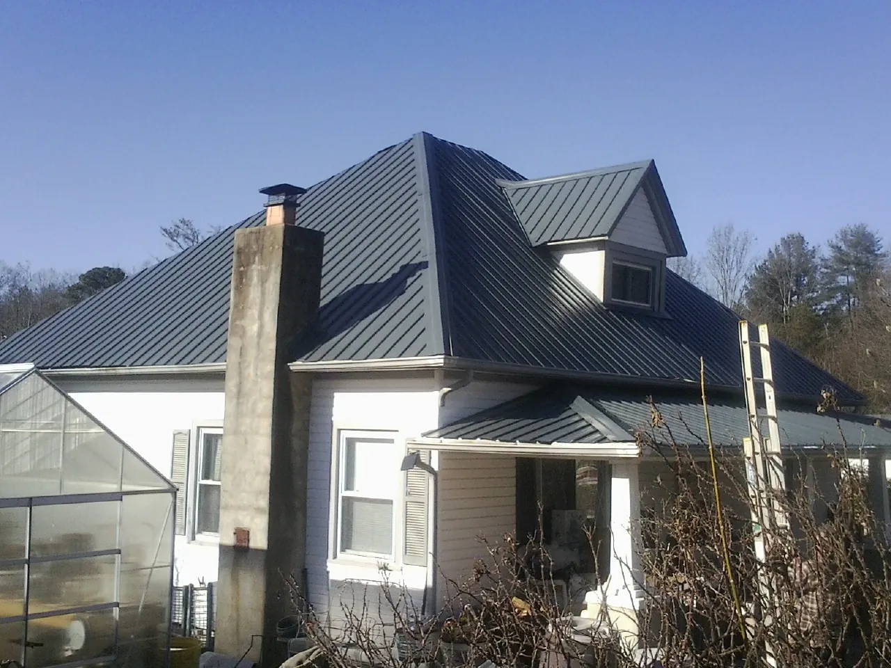Dark blue standing seam metal roof on a white farmhouse with dormer — Slate & Tile Roof Repair by Roofing Brothers in Stony Brook