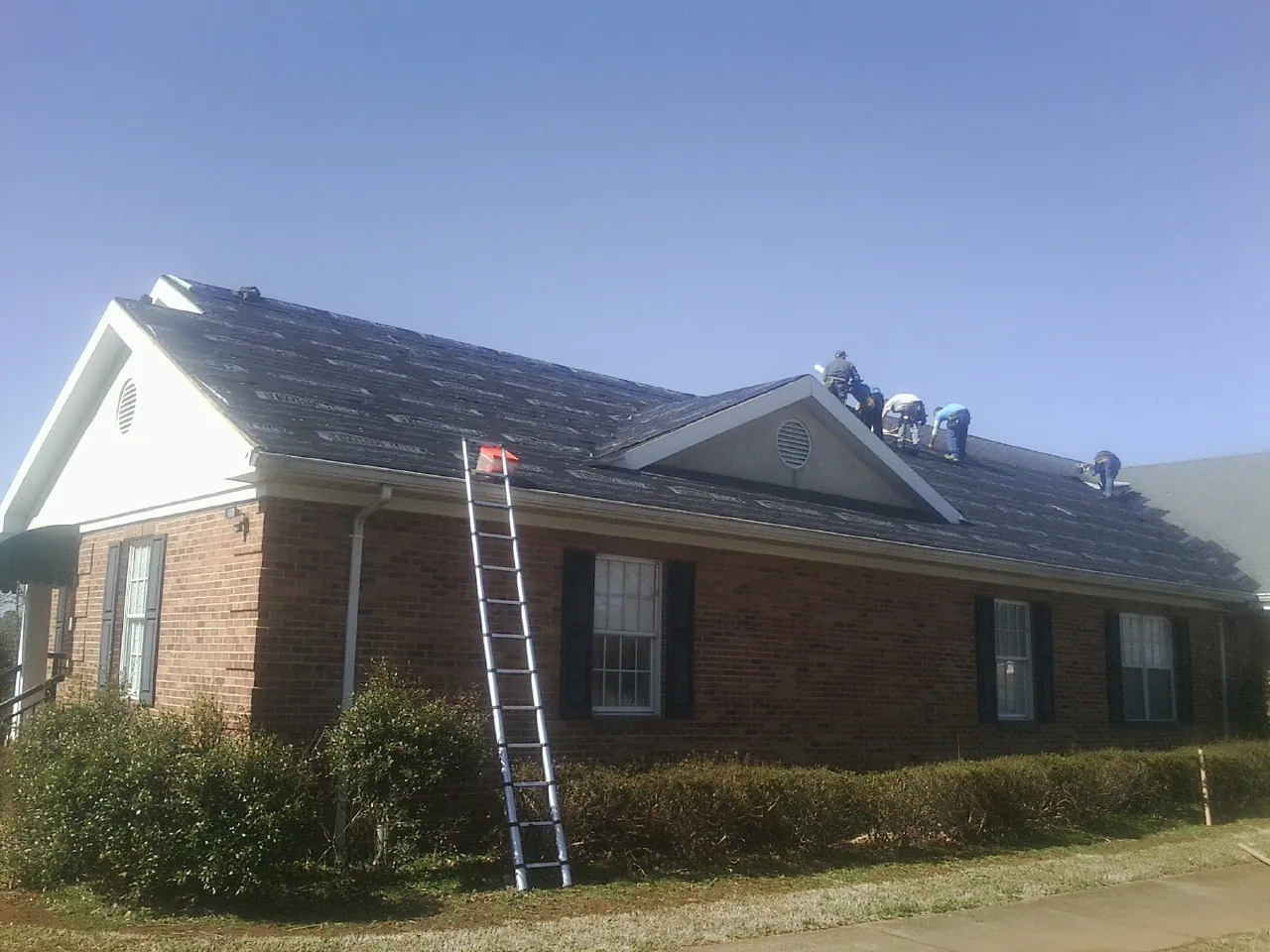 Crew tearing shingles off a brick ranch roof with a ladder set — Metal Roof Repair work by our crew in Stony Brook