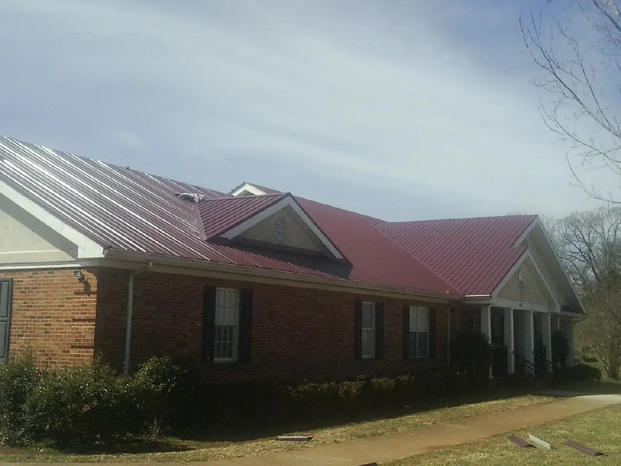 Red metal roof with gabled entries on a long brick building, from a Hail Damage Roof Repair job in Stony Brook