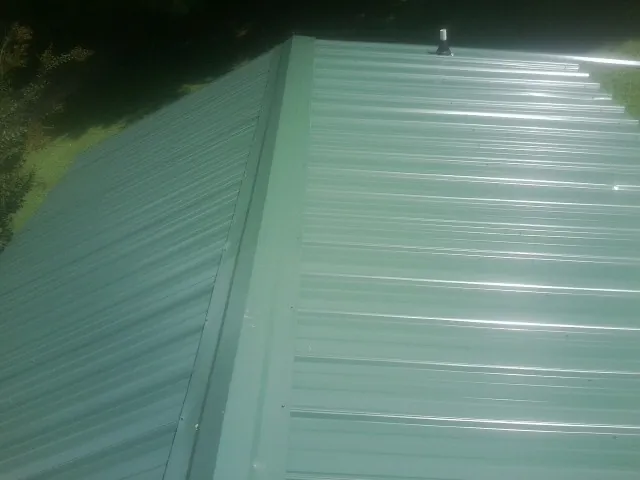 New green metal panels meeting at the ridge of a roof — Flat Roof Repair work by our crew in Stony Brook