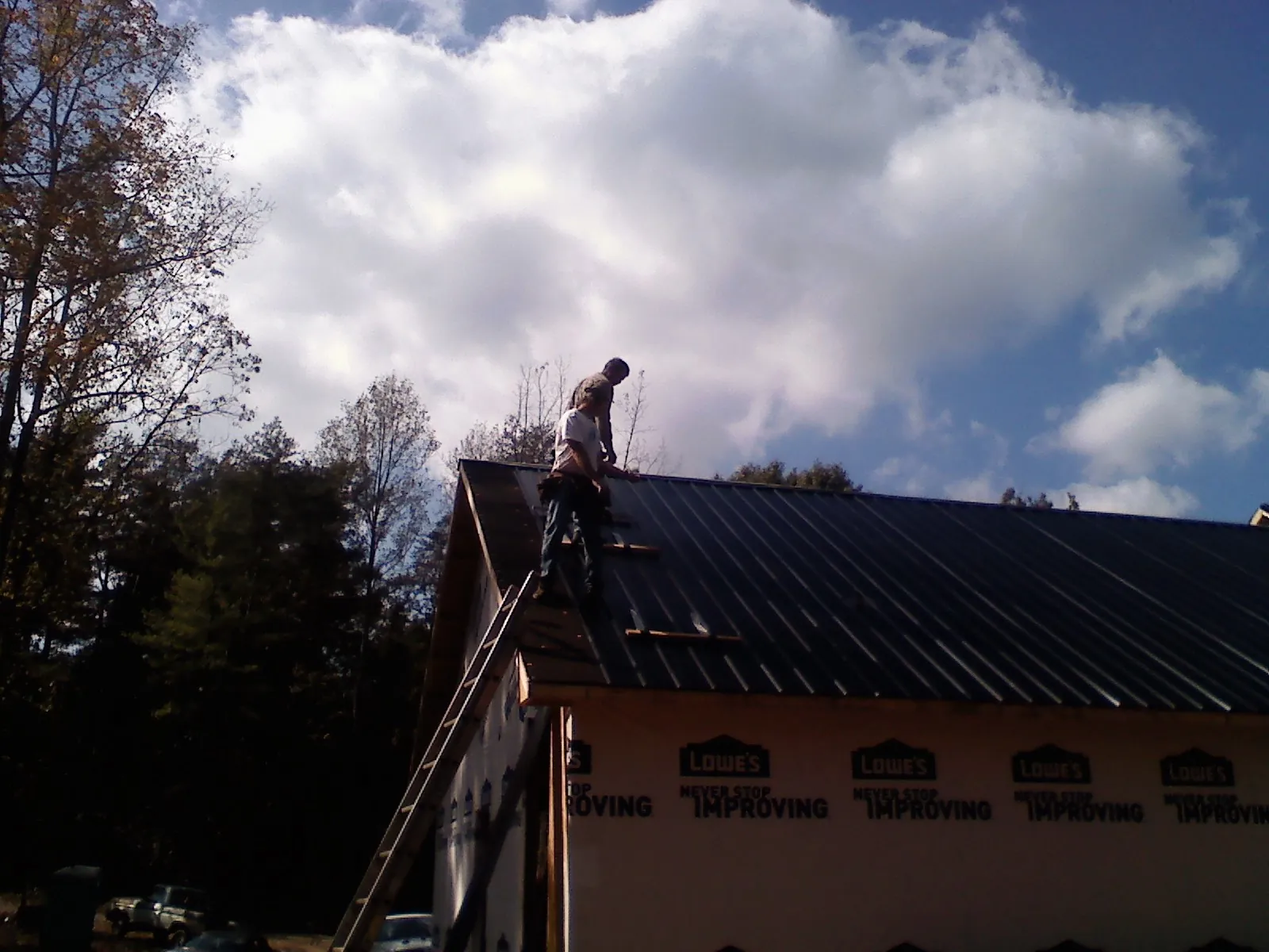 Roofer fastening dark metal panels high against a cloudy sky, from a Roof Inspection job in Stony Brook