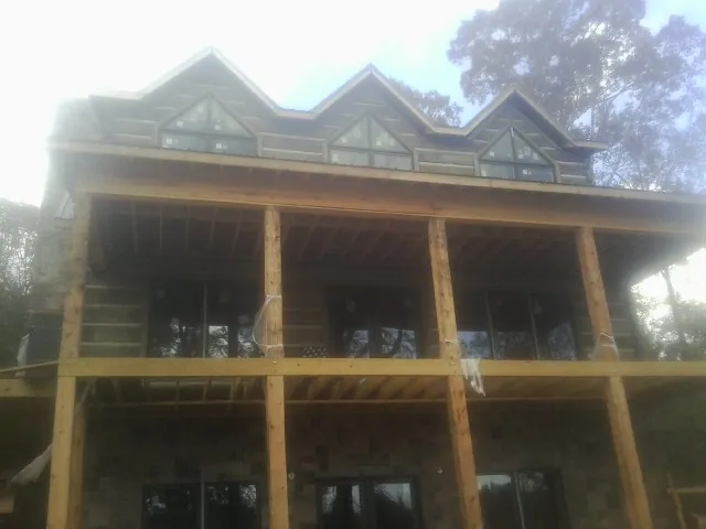 Dormers and porch framing on a large log home under construction — Roof Coating work by our crew in Stony Brook