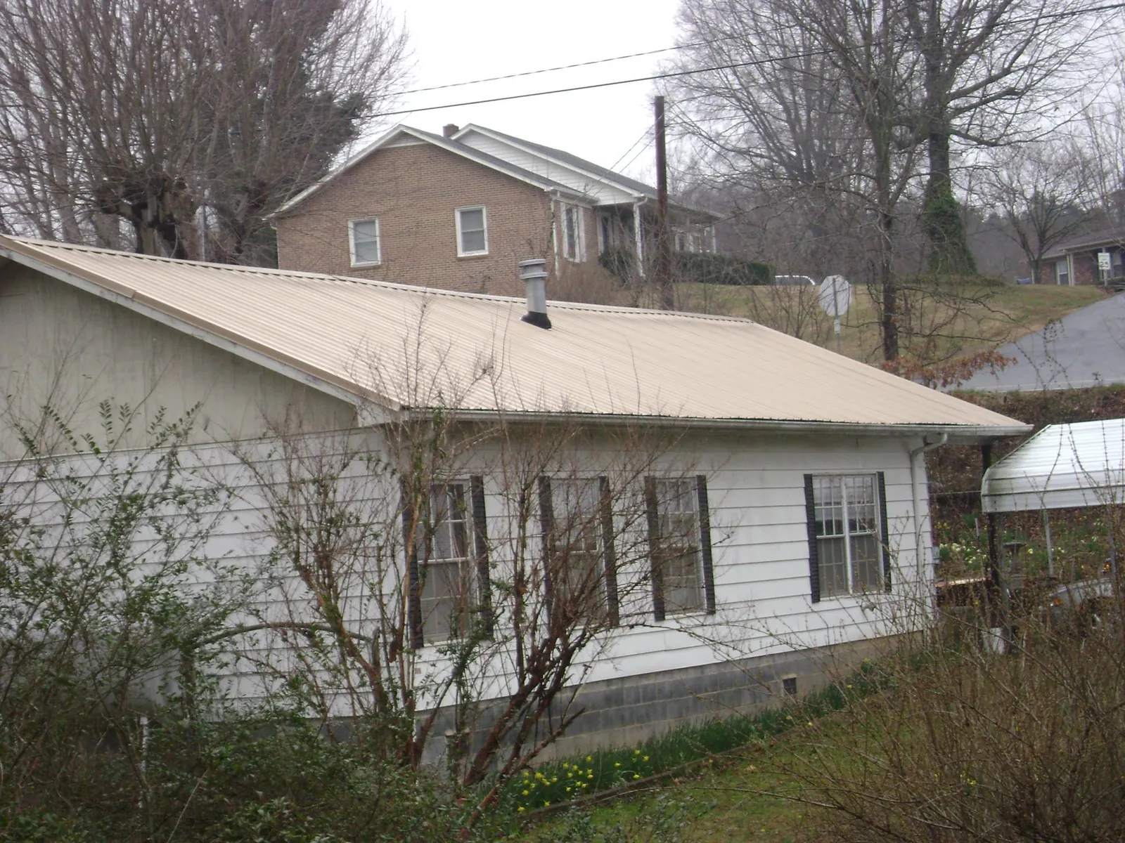 Tan metal roof on a white sided house set into a hillside — Commercial Roofing by Roofing Brothers in Stony Brook