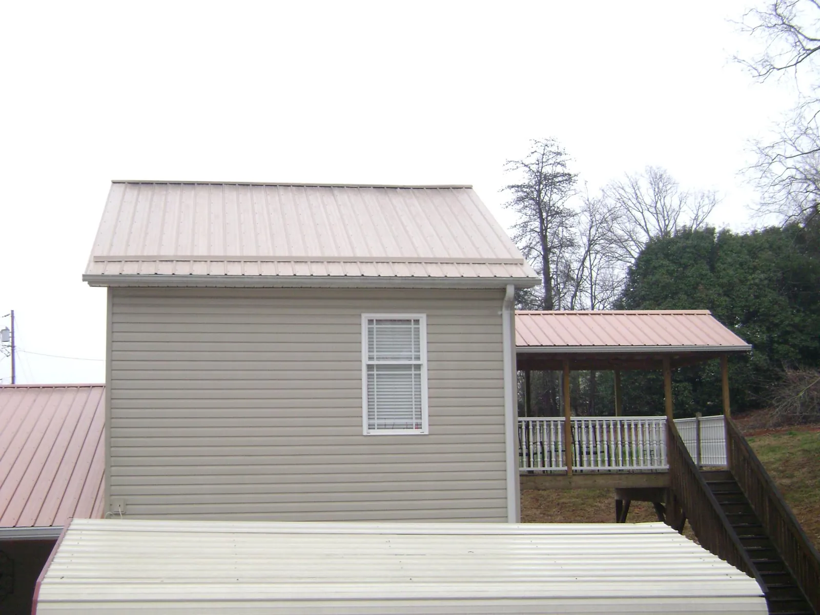 Tan metal roofs on a two story addition and attached porch, from a Roof Replacement job in Stony Brook